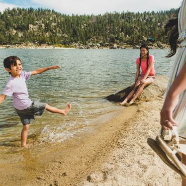 Un niño chapotea en el agua mientras juega en la orilla del lago Big Bear. Su hermana mayor y su madre miran.