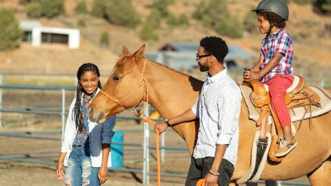 Una madre y su padre guían a un caballo mientras su hijo disfruta de un paseo a caballo.