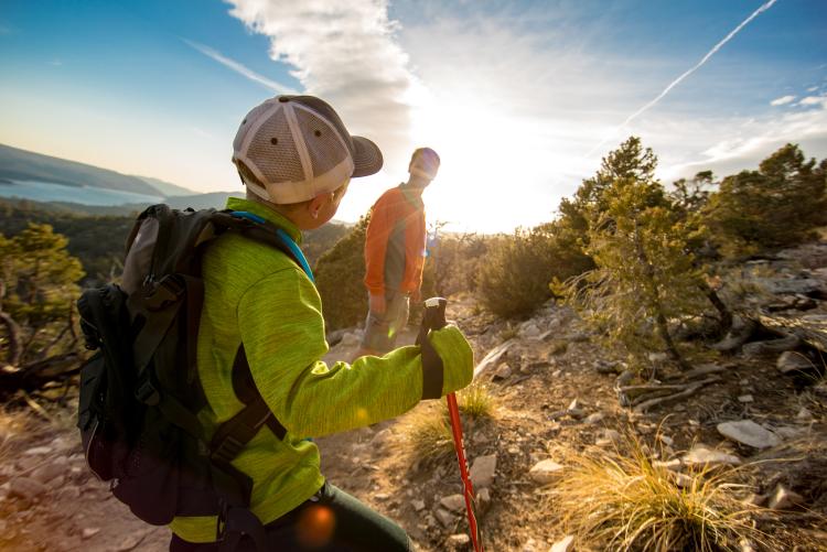 A photo of a father and son hiking on a trail during the sunset, the lake and mountains visible in the far distance.