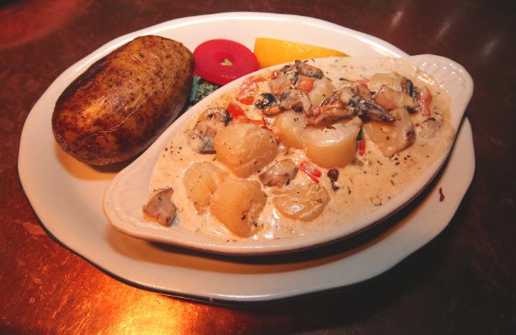 A photo of a dish at Captain's Anchorage, there are scallops in a cream sauce, baked potato, and vegetables.
