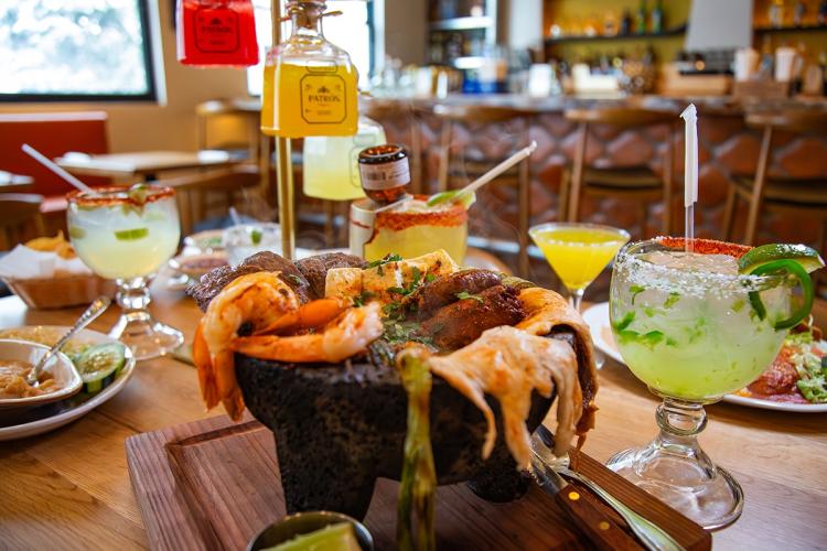 Un molcajete rodeado de otros platos típicos de la cocina mexicana en el restaurante «Rosa's» de Big Bear Lake; al fondo se ve una torre de botellas de tequila.
