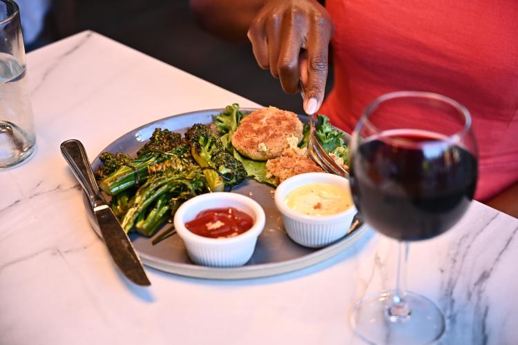 Una comensal corta su comida servida en el restaurante Stella Luna en Big Bear Lake, CA. Se sirve una copa de vino tinto.