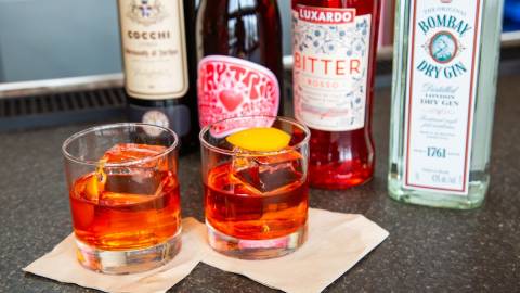 Una foto de un cóctel Negroni: es transparente, de color rojizo, y tiene una rodaja de naranja sobre un cubito de hielo.