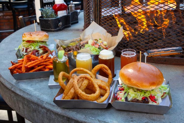 Una foto de hamburguesas y cervezas en Rock Burgers & Brews: hay patatas fritas de boniato y aros de cebolla en una caja con forma de concha.