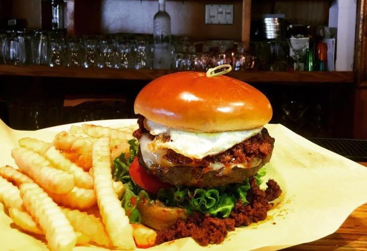 Hamburguesa Santana y Maverick con queso mozzarella, un huevo frito y una guarnición de patatas fritas.