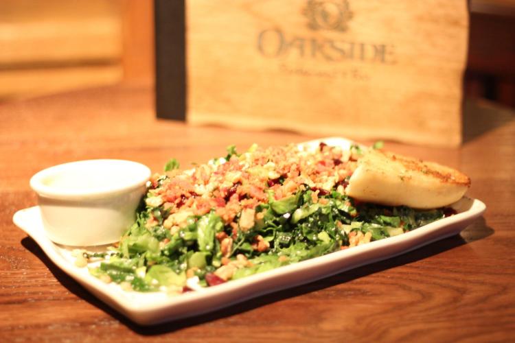 Un plato con ensalada, un trozo de pan y una taza de aderezo del restaurante Oakside en Big Bear Lake, CA.