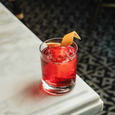 Una foto de un cóctel Negroni: es de color rojo cereza y tiene una rodaja de piel de naranja en la parte superior.