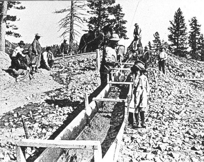 Fotografía en blanco y negro de buscadores de oro en un arroyo artificial.