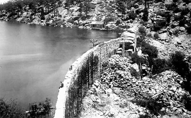 un hombre sentado en el borde de la primera presa de piedra de Big Bear Lake, frente a Big Bear Lake antes de 1911