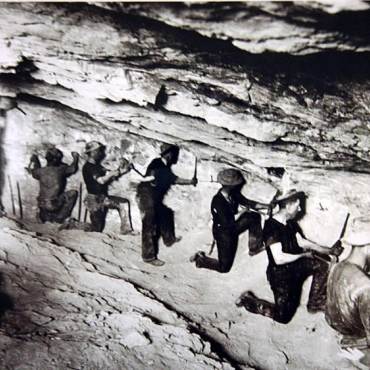 Fotografía en blanco y negro de un grupo de buscadores de oro en una cueva, utilizando cinceles para buscar en la roca.