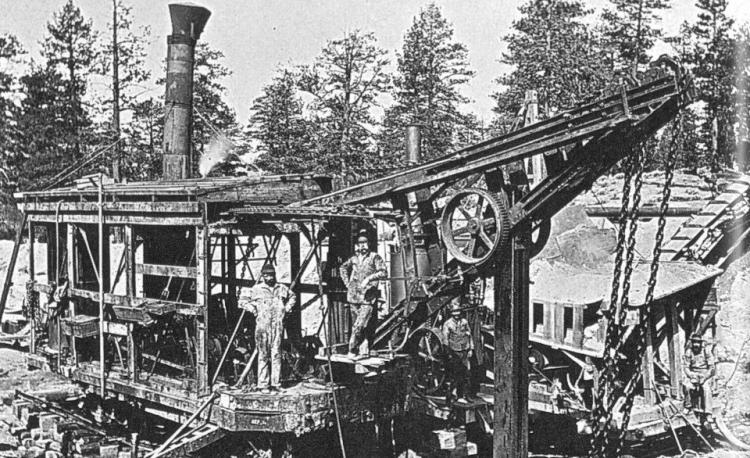 Una foto en blanco y negro de trabajadores junto a una máquina con cadenas y correas, con el escape saliendo por la parte superior de la máquina.