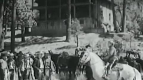 Foto en blanco y negro de un grupo de colonos de Big Bear, uno de ellos está montado en un caballo blanco, al fondo hay una casa.
