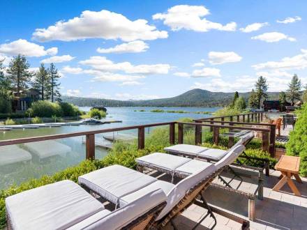 Cuatro tumbonas frente al lago Big Bear desde la terraza de una casa de vacaciones. Se ven montañas boscosas y el cielo azul.