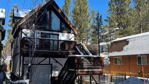 Una cabaña cubierta de nieve: cuenta con un garaje y unas escaleras exteriores que suben a la segunda planta, donde hay grandes ventanales.