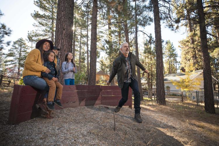 Una familia observa cómo su padre lanza una herradura en un pozo al aire libre en Big Bear Lake, California. Alojamiento en Big Bear.