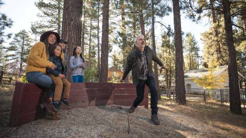 Una familia observa cómo su padre lanza una herradura en un pozo al aire libre en Big Bear Lake, California. Alojamiento en Big Bear.