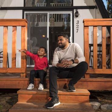 Un padre y su hijo se sientan en las escaleras de su casa de alquiler en Big Bear Lake y admiran el bosque que les rodea.