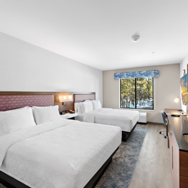 En el interior de una habitación de hotel hay dos camas grandes, un lavabo y estanterías, un televisor y un escritorio.