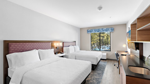A hotel room interior, there are two large sized beds, a in counter sink and shelves, a television, and a desk workspace.
