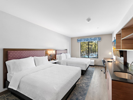 A hotel room interior, there are two large sized beds, a in counter sink and shelves, a television, and a desk workspace.
