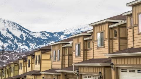 Una foto de casas adosadas, hay montañas cubiertas de nieve y una ciudad a lo lejos.