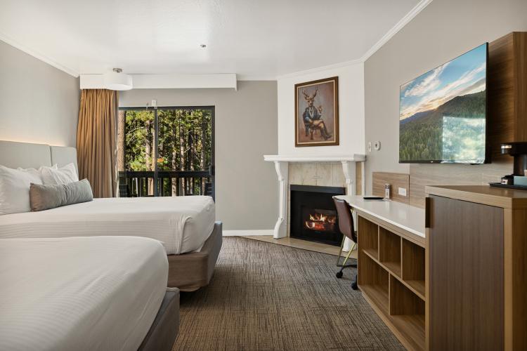 En una foto del interior de una habitación del Chateau Big Bear, hay un televisor, dos camas bien hechas, una mininevera y una chimenea.