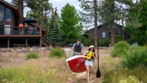Una pareja lleva tablas de paddle al lago Big Bear desde su casa de alquiler vacacional frente al lago.