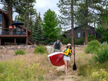 Una pareja lleva tablas de paddle al lago Big Bear desde su casa de alquiler vacacional frente al lago.