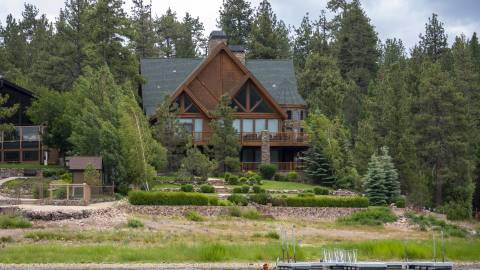 Una hermosa casa marrón se asienta en la orilla del lago Big Bear. Un kayakista pasa remando por el agua.