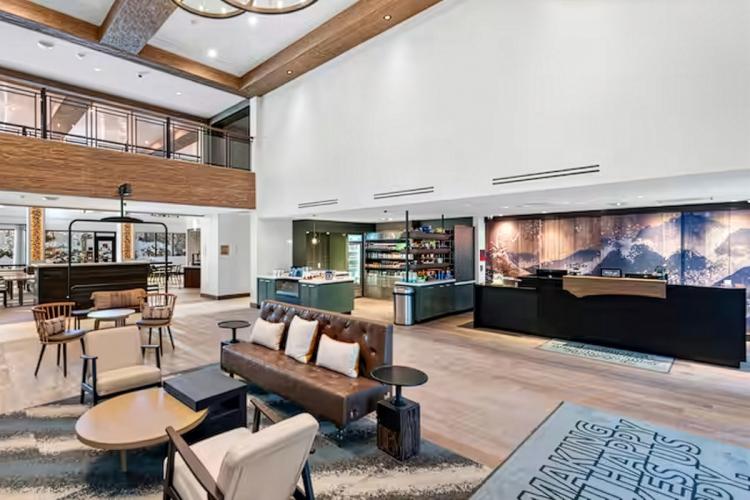 Una imagen del interior de Home2 Suites: hay un salón diáfano con sofás, sillas y una barra con numerosas estanterías para bebidas.