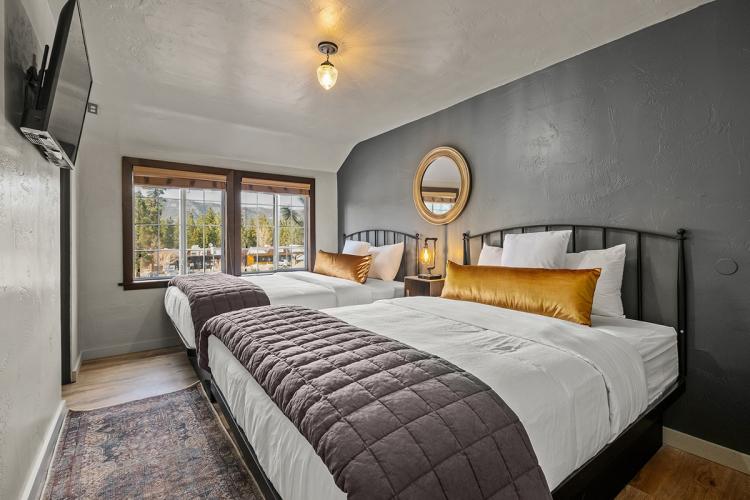 Una foto del interior de «The Lodge», en Sessions Retreat: hay dos camas mullidas, una ventana, una mesita de noche y un televisor.