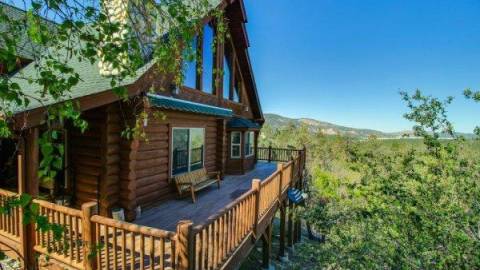 Una cabaña de madera rodeada de verdes robles. Una gran cubierta envuelve la casa.